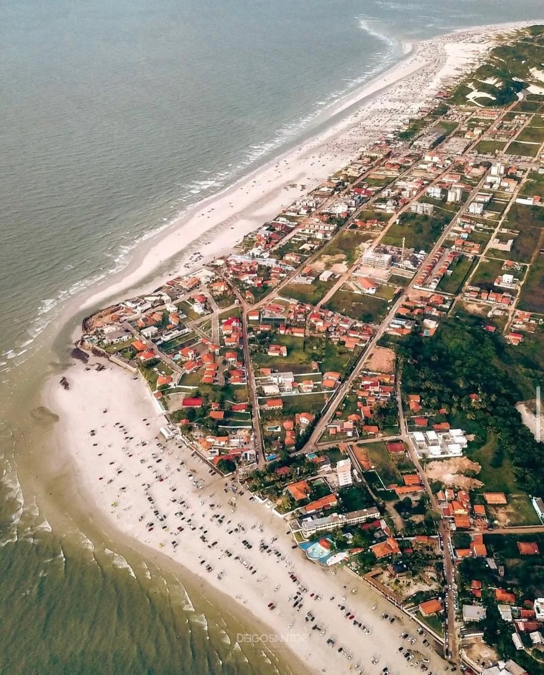 Roteiro Completo Praia do Atalaia Salinas - O que fazer e como chegar Vista panorâmica da Praia do Atalaia em Salinas com carros estacionados na areia e mar ao fundo durante o pôr do sol.